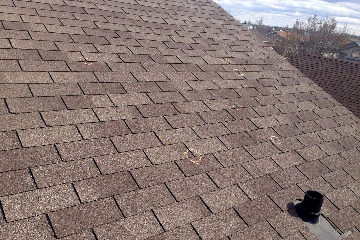 Roof inspection reveals a close up of an asphalt roof with indications of broken shingles and poor nail-head placement circled