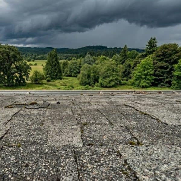 Dark storm clouds over a rooftop with lush green trees in the background.